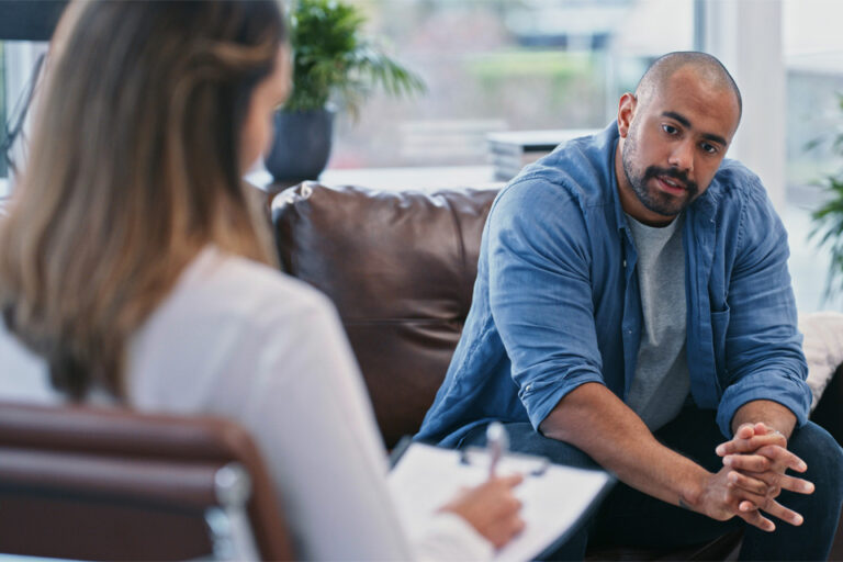 man in an addiction counseling session while a woman counselor takes notes on a clipboard