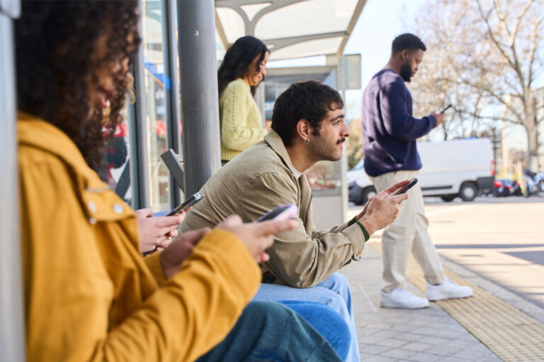 group of people looking at their smartphones waiting at a bus stop
