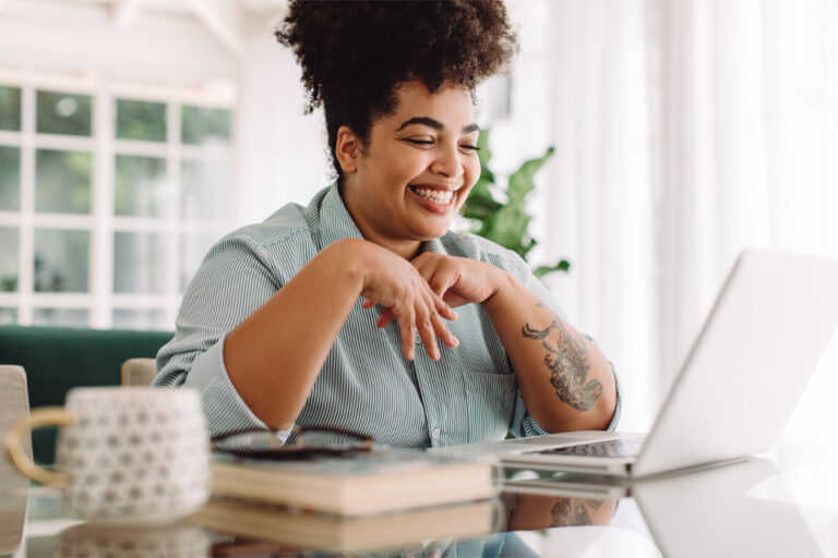 woman smiling while working on a laptop - Referring a Patient to a CMS Clinic?